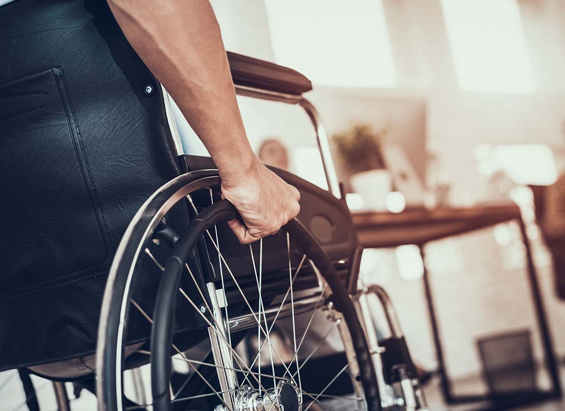 Long-Term Disability Insurance - Close-up of a Man Using a Wheelchair in the Doctor’s Office with the Reception Desk Area in the Distance